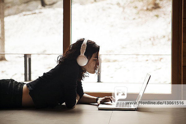 Seitenansicht einer Teenagerin  die einen Laptop benutzt  während sie zu Hause auf dem Boden liegt