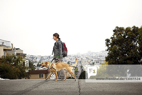 Side view of woman and dog walking on street against cityscape