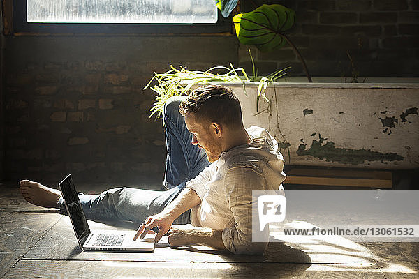 Mann benutzt Laptop-Computer  während er zu Hause auf dem Boden liegt