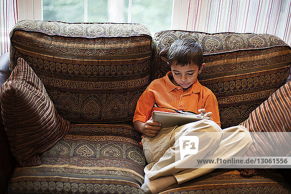 Junge benutzt Tablet-Computer  während er zu Hause auf dem Sofa sitzt
