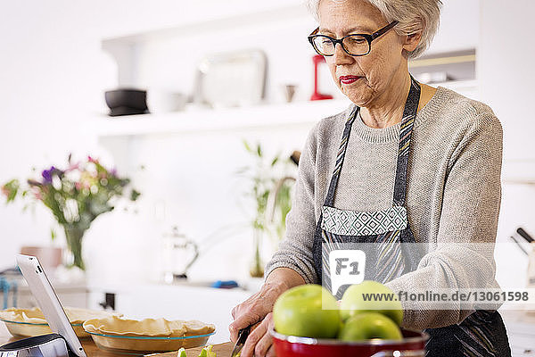Senior woman slicing apples at table in kitchen