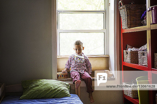 Portrait of boy sitting on window sill in bedroom at home