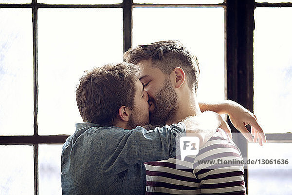 Zärtliches schwules Paar küsst sich zu Hause am Fenster