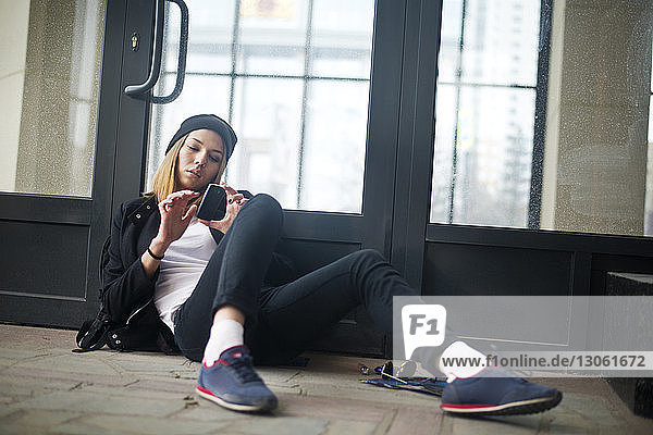 Female hipster using phone while relaxing against door