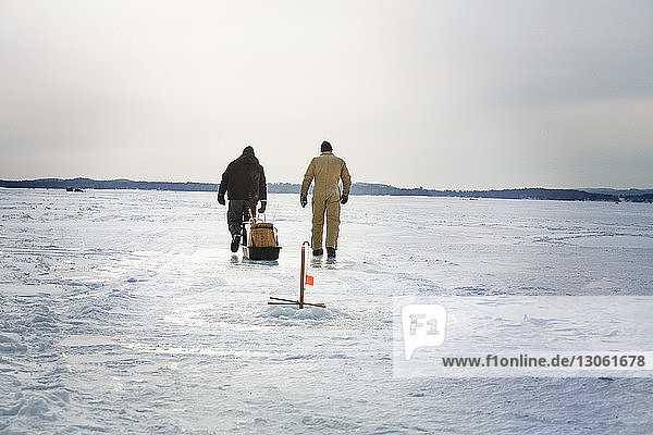 Rückansicht von Freunden,  die auf einem zugefrorenen See vor bewölktem Himmel spazieren gehen