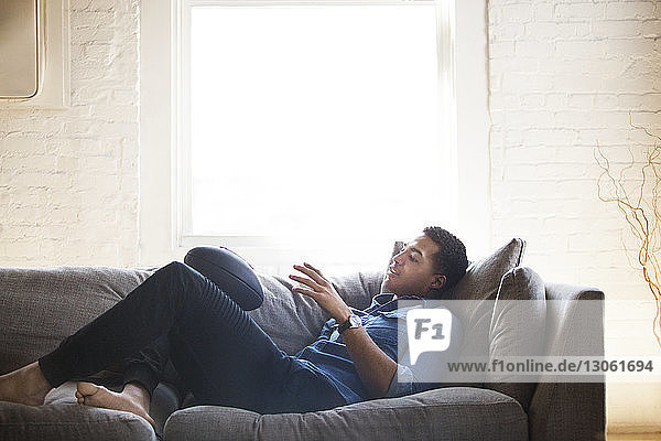 Man holding rugby ball while lying on sofa at home