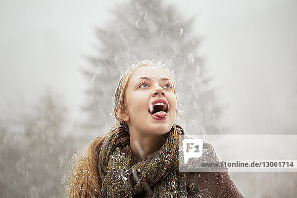 Woman sticking out tongue at forest during winter