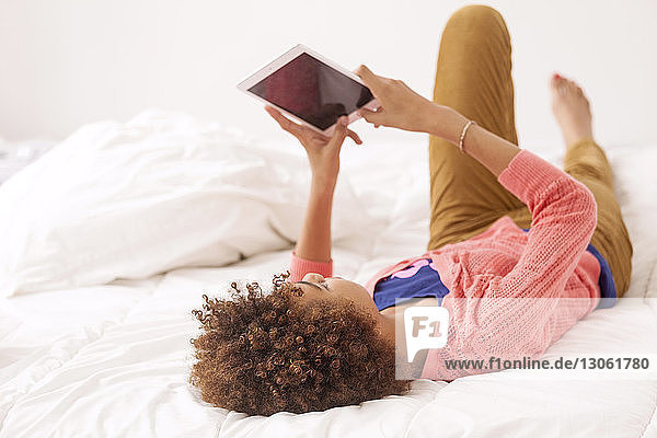 Mädchen benutzt Tablet-Computer  während sie zu Hause auf dem Bett liegt