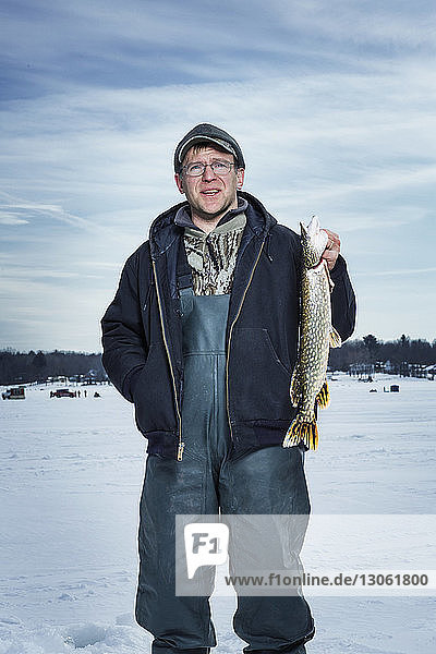 Lächelnder Mann hält Fisch und steht auf gefrorenem See