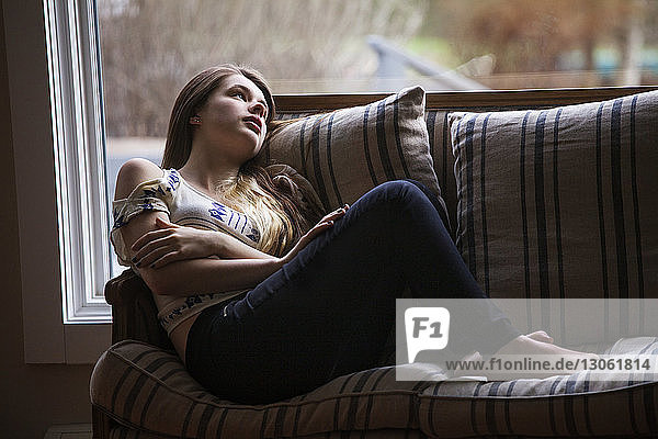 Mädchen schaut weg  während sie sich zu Hause auf dem Sofa entspannt