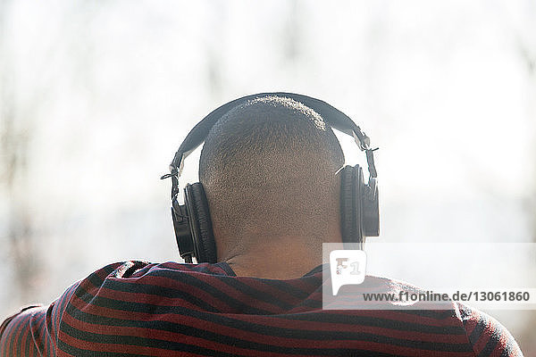 Rückansicht eines Mannes  der zu Hause über Kopfhörer Musik hört