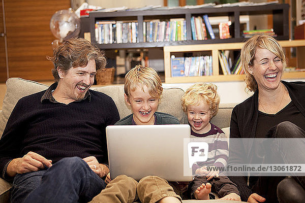 Geschwister benutzen Laptop  während sie zu Hause mit den Eltern auf dem Sofa sitzen