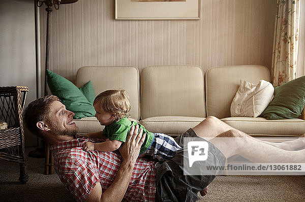 Seitenansicht eines Vaters  der zu Hause mit einem kleinen Jungen auf einem Teppich spielt