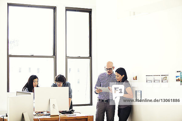 Geschäftsmann und Geschäftsfrau benutzen Tablet  während ihre Kollegen im Büro am Computer arbeiten