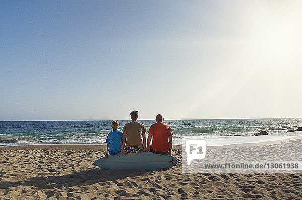 Rückansicht einer Familie  die auf einem Surfbrett am Strand vor klarem Himmel an einem sonnigen Tag sitzt