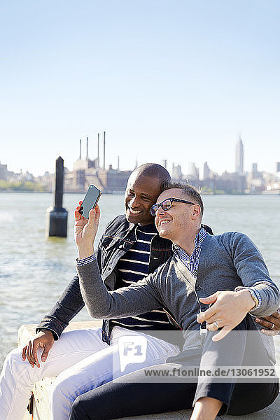Glückliche Freunde nehmen Selfie am Fluss gegen den klaren Himmel an einem sonnigen Tag