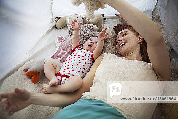 Mother playing with daughter while lying in tent at home