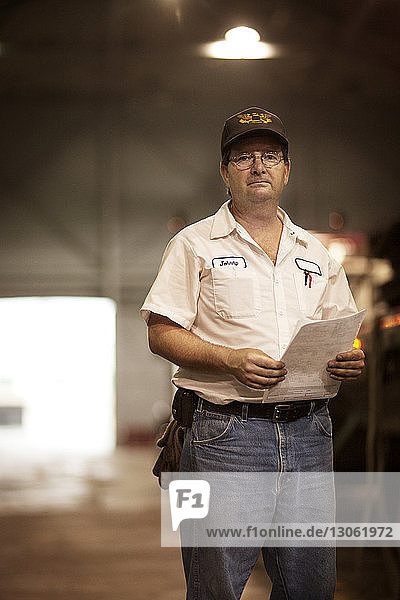 Portrait of man holding document while standing in industry