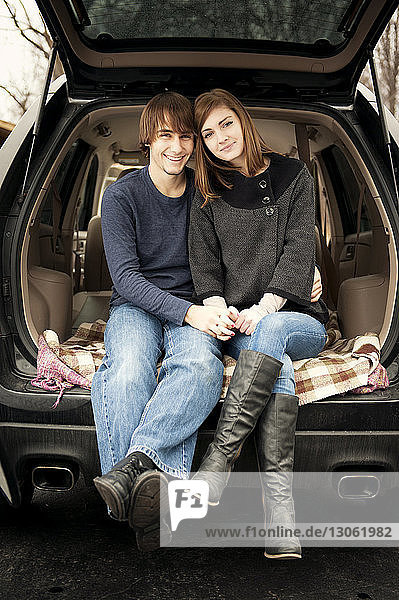 Portrait of happy young couple sitting car trunk