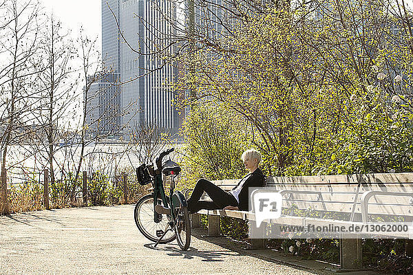 Frau ruht auf Bank neben geparktem Fahrrad am Fluss in der Stadt