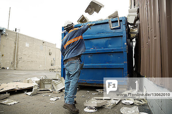 Rückansicht eines männlichen Arbeiters  der in einer Recycling-Anlage Müll in einen Container wirft