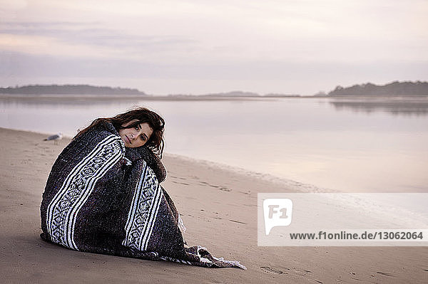 Portrait of woman wrapped in blanket sitting on beach