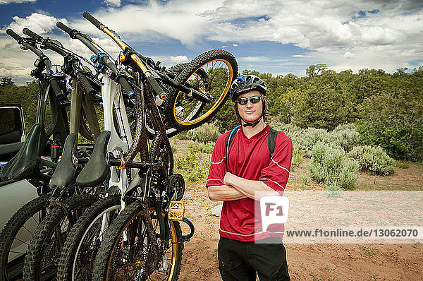 Portrait of mountain biker with arms crossed standing against cloudy sky