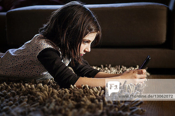 Girl using mobile phone while lying on rug at home