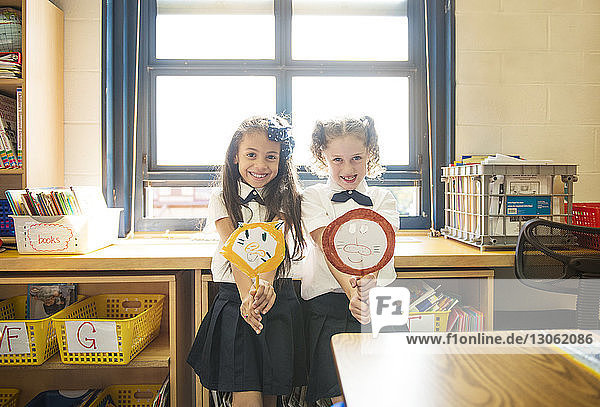 Portrait of happy schoolgirls holding craft products while standing in classroom