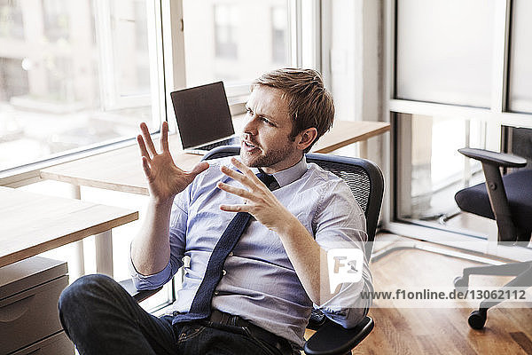 Businessman gesturing while sitting on chair at office