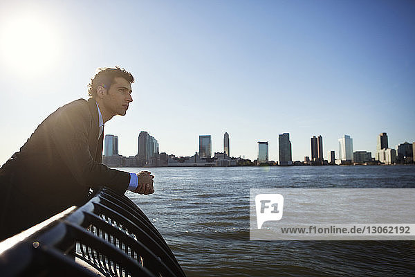Side view of businessman standing at railing by river against clear sky