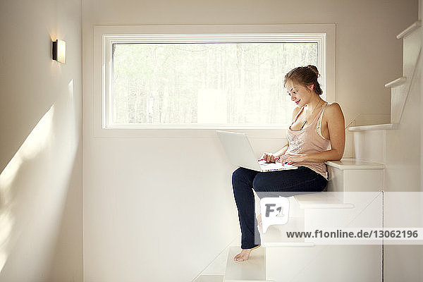 Happy woman using laptop computer while sitting on steps