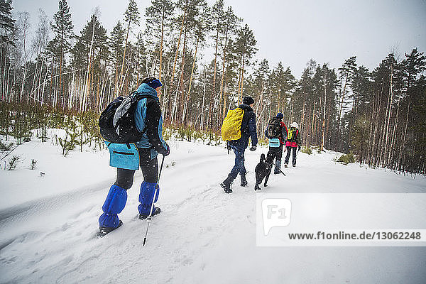 Rückansicht von Freunden  die einen Rucksack tragen  während sie auf einem schneebedeckten Feld gehen