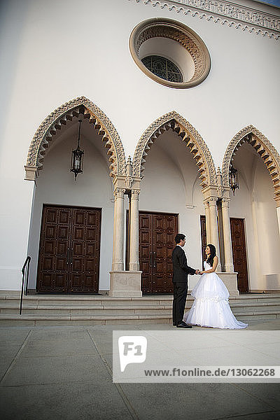 Braut und Bräutigam halten sich an den Händen  während sie vor der Kirche stehen