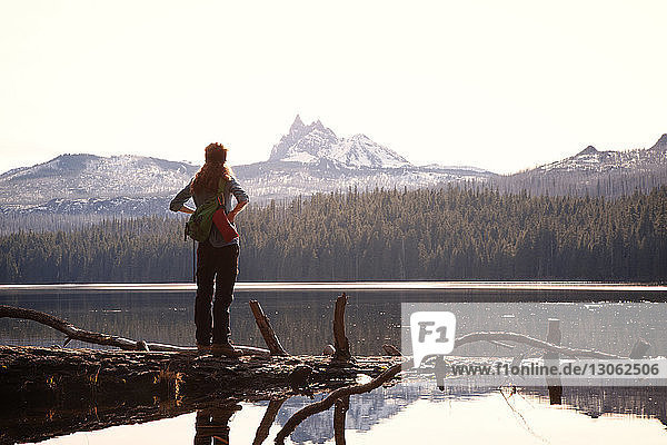 Female hiker standing at lakeshore against mountains