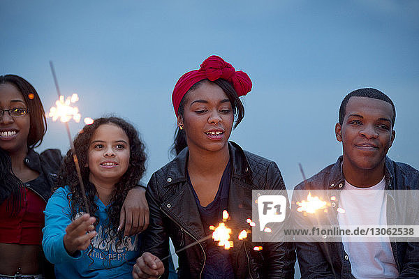 Friends holding sparklers against sky