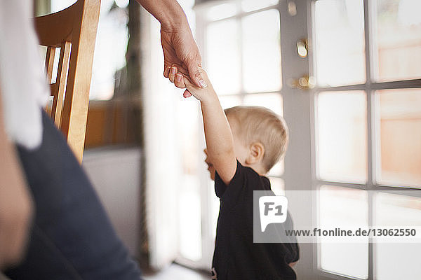 Ausgeschnittenes Bild einer Mutter  die zu Hause die Hand des Sohnes hält