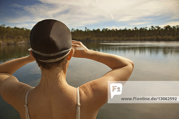 Rear view of woman wearing swimming cap standing against lake