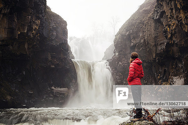 Weibliche Wanderin betrachtet Wasserfall  während sie im Wald auf einem Felsen steht