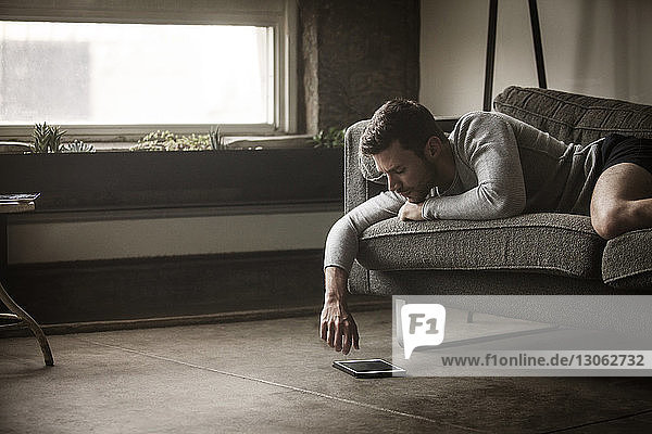 Mann schaut auf Tablet-Computer  während er auf dem Sofa liegt
