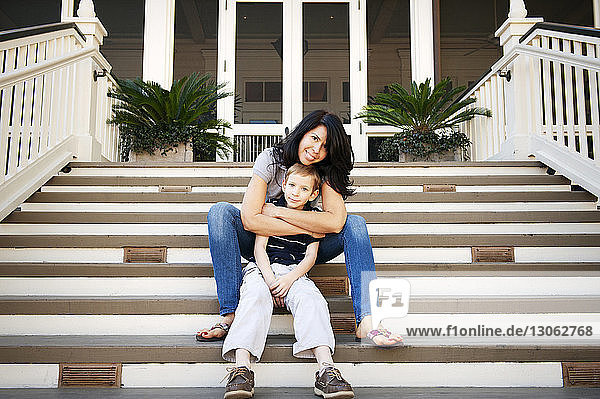 Porträt einer glücklichen Mutter  die ihren Sohn umarmt  während sie auf einer Treppe sitzt