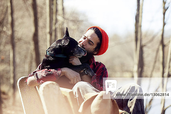 Anhänglicher Mann schaut Hund an  während er während des Urlaubs im Wald auf einer Bank sitzt