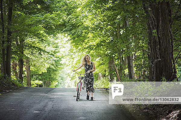 Frau mit Fahrrad auf Straße inmitten von Bäumen