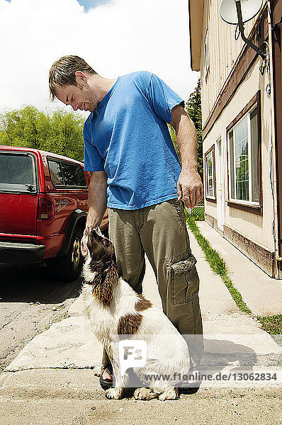 Man playing with dog while standing on footpath against building