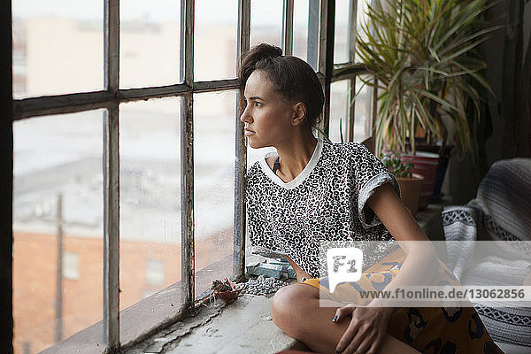 Woman looking through window while sitting at home