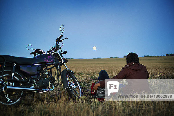 Rückansicht von Vater und Sohn  die mit dem Motorrad auf dem Feld gegen den Himmel sitzen