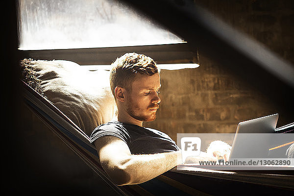 Mann benutzt Laptop-Computer  während er sich in der Hängematte entspannt
