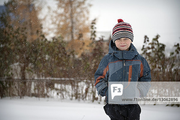Portrait of smiling boy in warm clothing standing on snow covered field