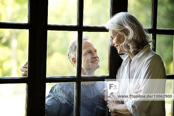 Lächelnde ältere Frau betrachtet Mann durch Fenster gesehen