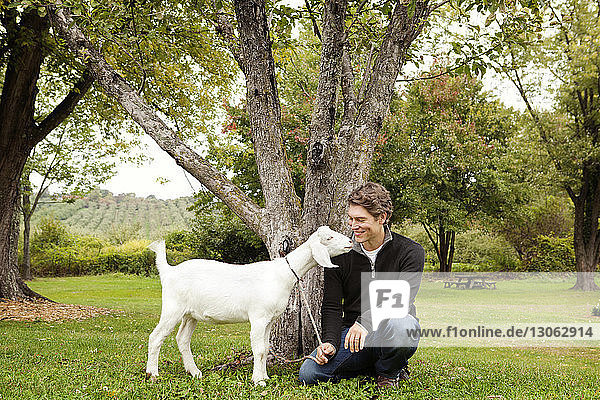 Happy man with goat on grassy field